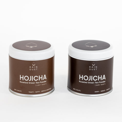 Two containers of Rain Dust Premium Hojicha roasted green tea powder on a white background