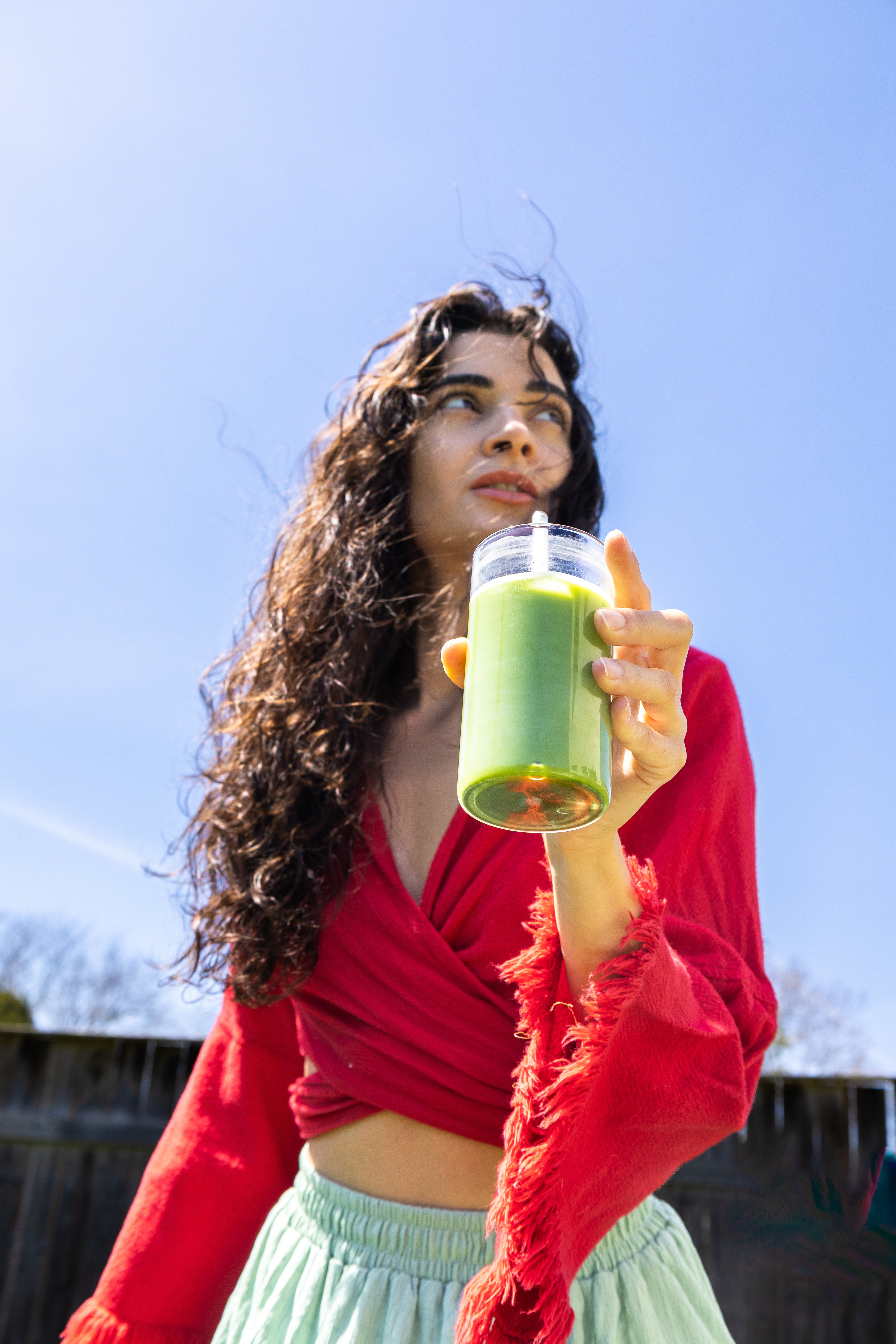 Woman enjoying a premium Japanese matcha latte outdoors under a clear blue sky