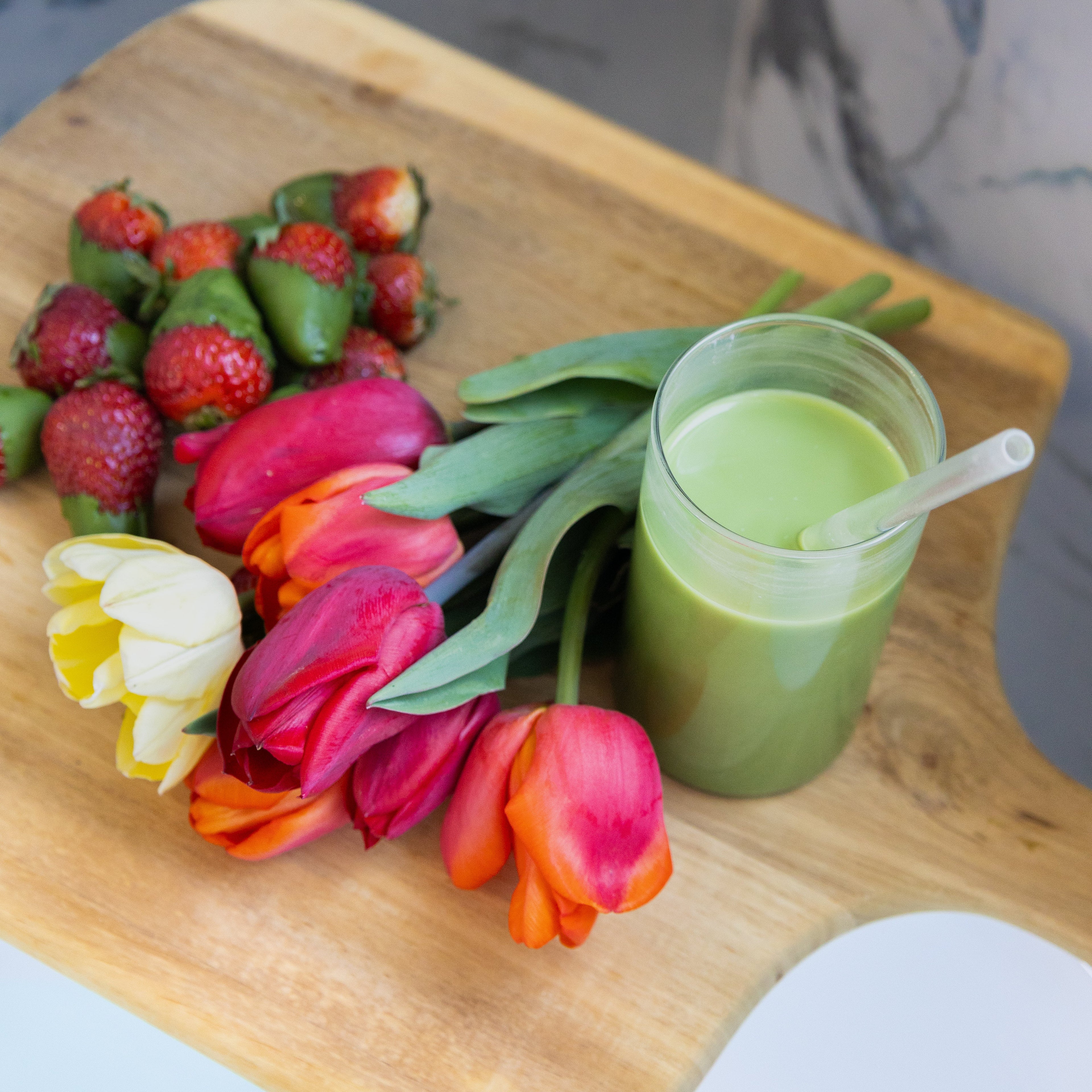 premium matcha in a glass with a straw on a wooden board with matcha strawberries and tulips.